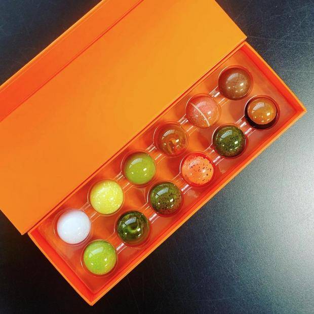 A rectangular orange box of bonbons with the lid open, the bonbons are all round and brightly colored