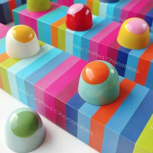 A collection of narrow, colorful, striped boxes with round molded bonbons decorated with large dots