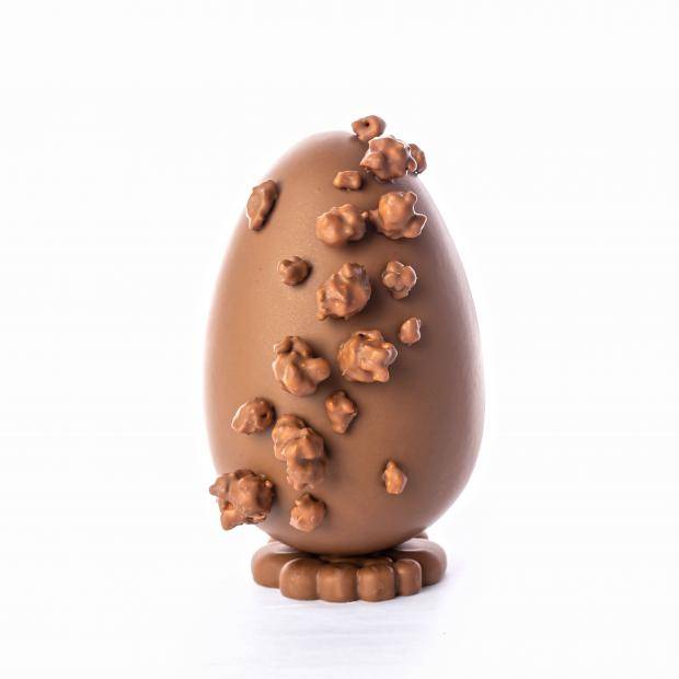 ovo de chocolate ao leite em pré de frente com pipocas banhadas no chocolate grudadas na casca