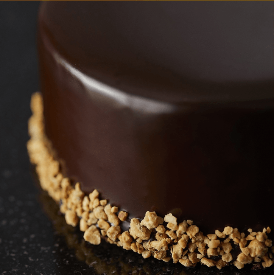 Exterior of a ganache-covered chocolate cake garnished with chopped nuts
