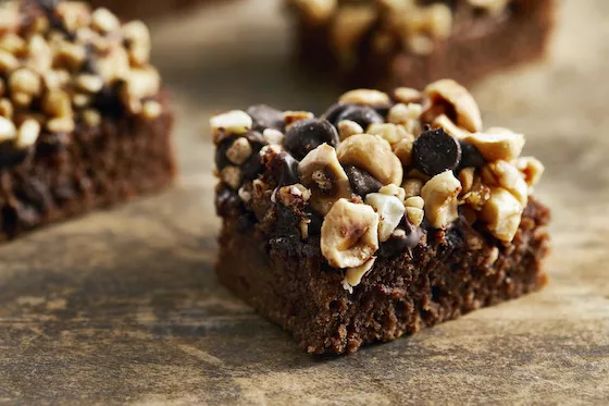 Brownies topped with chopped nuts and chocolate chunks on a stone-like surface
