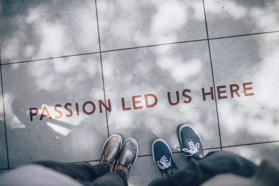 Top-down shot of two people with just feet/legs visible standing in front of "Passion led us here" printed on sidewalk