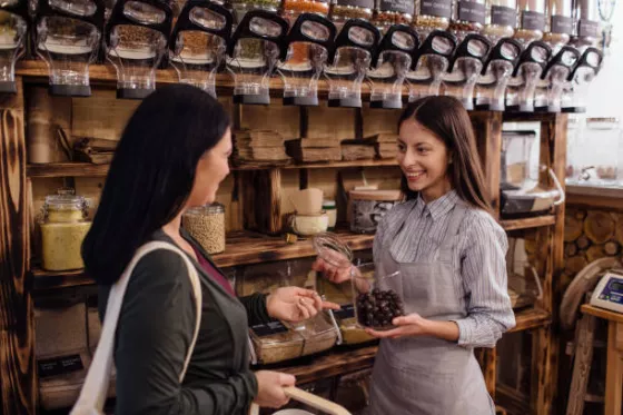 Two women in a chocolate shop, one is holding open a jar for the other