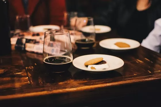 A table with glasses of dark beer next to plates with a chocolate, marshmallow, and cookie
