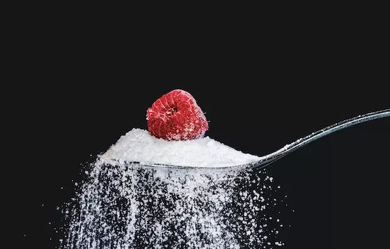 Uma colher cheia de açúcar com uma framboesa por cima