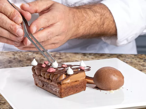 chef finalizando uma receita de brownie, colocando a decoração por cima da fatia que está no prato ao lado de uma bola de sorvete de chocolate