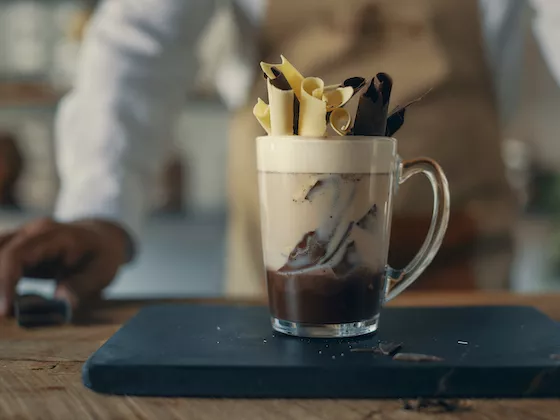 A layered chocolate coffee drink with dark and white chocolate curls