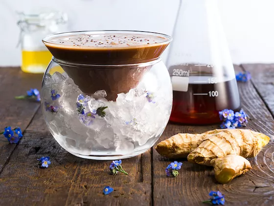 A Chocolate cocktail on a bed of ic with coffee and ginger in the background