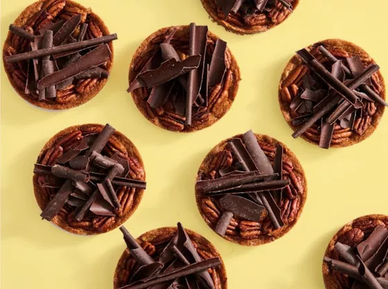 Top-down shot of multiple mini pecan pies topped with large chocolate shavings and whole pecans