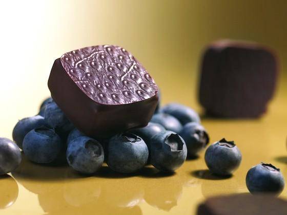 An enrobed bonbon sits on top of a pile of blueberries