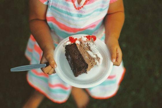 Looking down at a child holding a slice of chocolate cake on a white plate