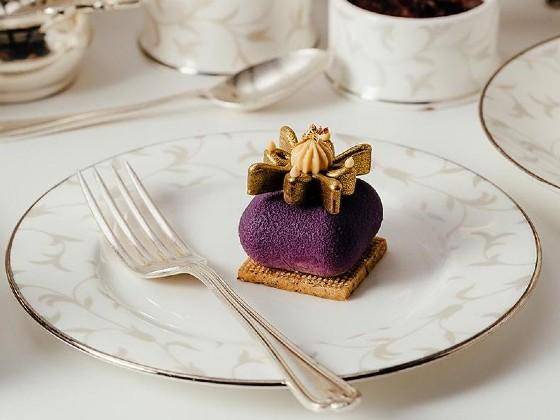 A purple petit gateau shaped like a cushion holds a gold chocolate crown