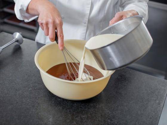 A chef mixes cream into melted chocolate to create a ganache