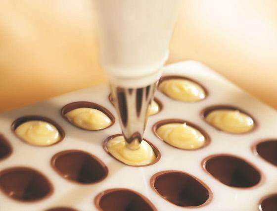 a light-colored filling being piped into dark chocolate shells