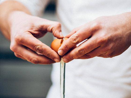 A chef cracks an egg into a container below